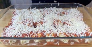 Glass baking dish with stuffed pasta shells, tomato sauce, and shredded cheese topping.